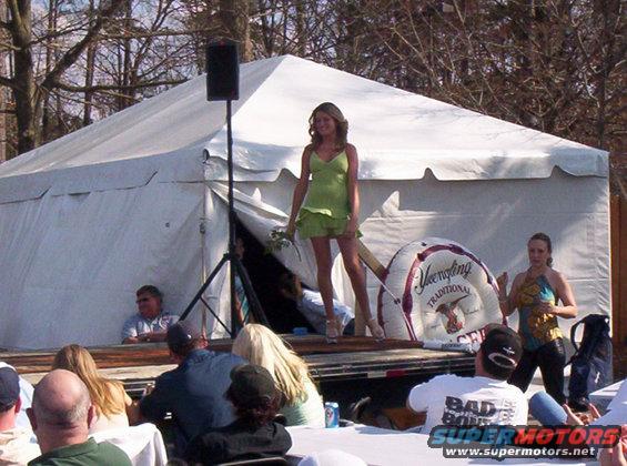 Woman in green dress on stage, people watching, tent behind