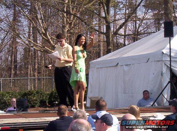 Man and woman on stage, woman waves; tent in background