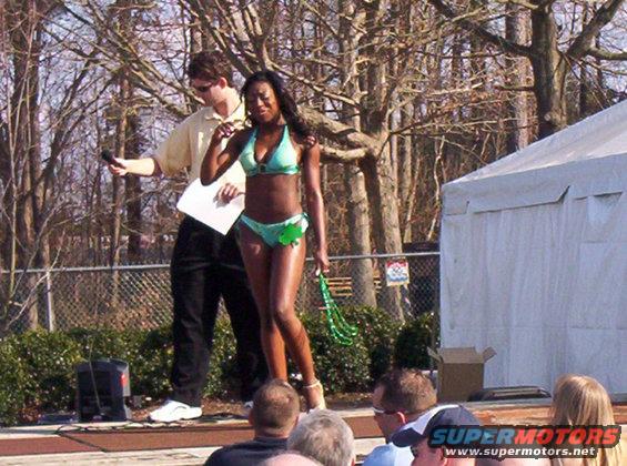 Woman in bikini on stage with a man holding a microphone and paper