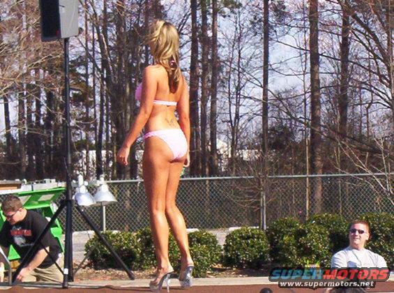Woman in pink bikini on stage with trees and a fence in the background