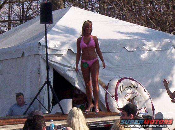Woman in pink bikini on stage with a tent behind her and a large inflatable ring