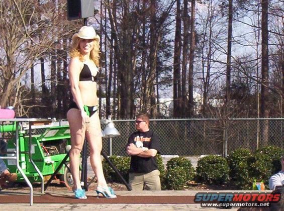 Woman in black bikini and cowboy hat on stage with a green generator behind her