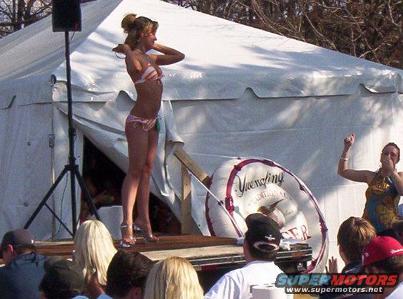 Woman in bikini on stage at outdoor event with audience watching