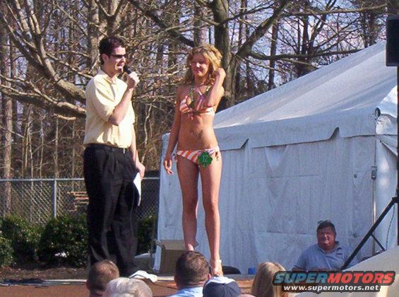 Bikini contest stage with a woman in an orange and white striped bikini and a man holding a microphone