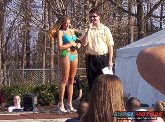 Woman in bikini on stage with announcer holding microphone