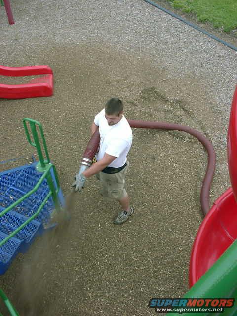 Man in white shirt and shorts using a blower hose on a playground