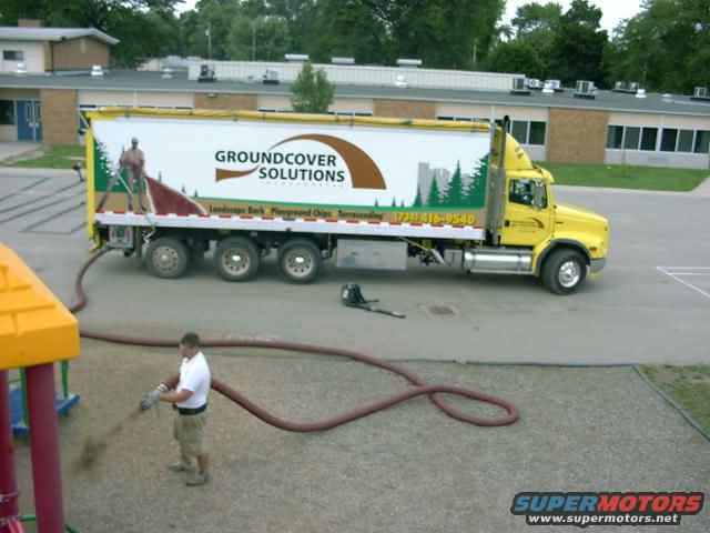 Yellow semi-truck with a white trailer displaying "GROUNDCOVER SOLUTIONS" logo, parked on asphalt