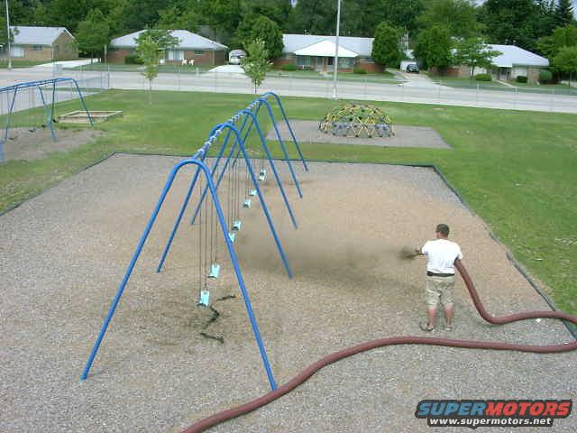 Playground scene with a person spraying a hose near swings