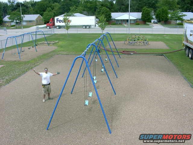Playground with swings, a geodesic dome climber, and a man standing with arms outstretched