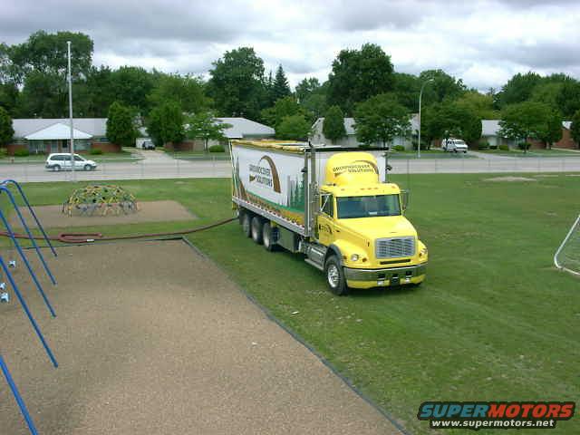 yellow semi-truck parked on grass, trailer has text on side