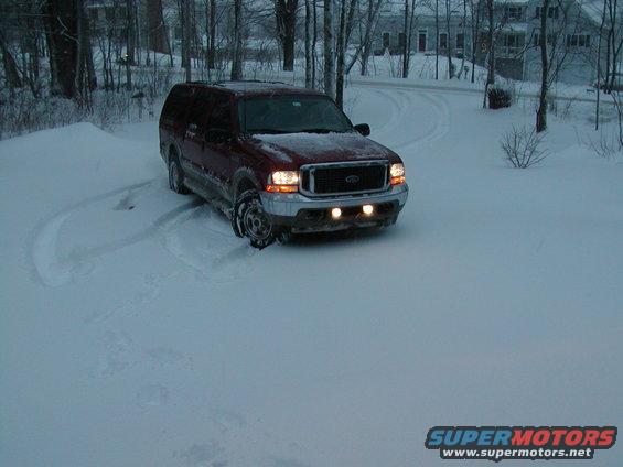 Maroon Ford Excursion in snow, front view, with headlights and fog lights on