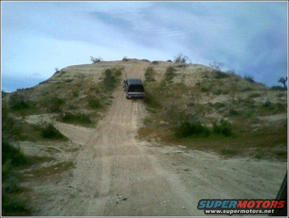 Dark pickup truck driving up a dirt hill