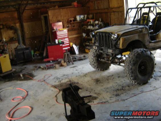 Modified off-road vehicle with large tires inside a garage. The vehicle is yellow and has a roll cage