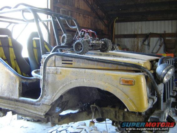 Yellow off-road vehicle with roll cage, mud-splattered, in a barn