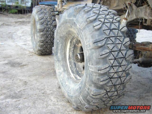 Two large, knobby off-road tires on a dirt surface, with suspension visible