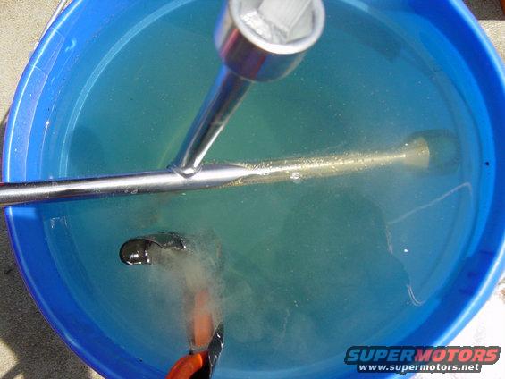 Socket wrench and metal part submerged in blue water inside a bucket. Text reads SUPERMOTORS