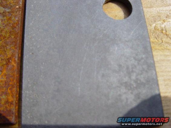 Close-up of a metal part with rust on one edge and a hole drilled in it