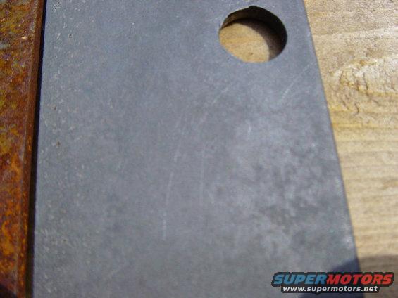 Rusted metal bracket with a circular hole drilled in it, resting on wood