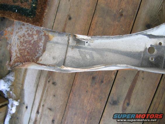 Rusted, bent metal car part on wooden planks with snow