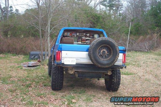 Rear view of a blue 1987 Ford Bronco with a spare tire mounted on the back. License plate reads 'BYON ASF'