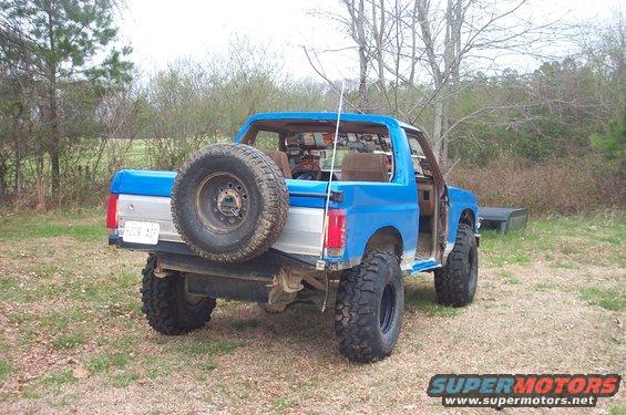 Blue Ford Bronco with spare tire on rear, lifted suspension, and open driver's door