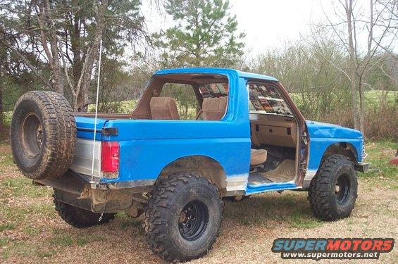 Blue 1987 Ford Bronco with spare tire on rear, lifted suspension, and removed doors