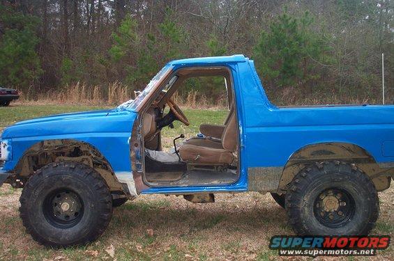 Side view of a blue SUV with doors removed, large tires, and exposed interior
