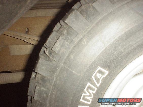 Tire with visible cracks and damage to the sidewall. Part of a vehicle's undercarriage is visible
