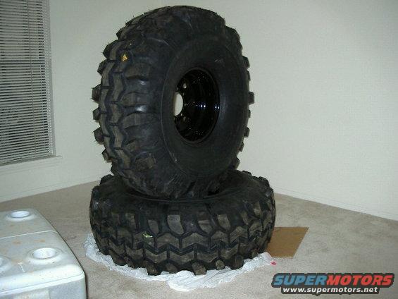 Two large off-road tires stacked indoors. One tire is on top of the other