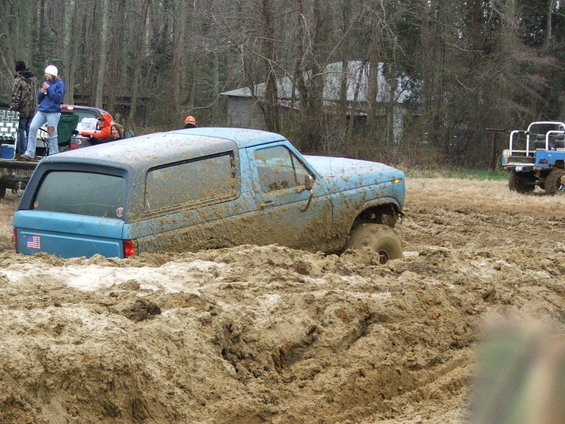 Blue SUV stuck deep in mud, front wheel submerged, rear tire visible