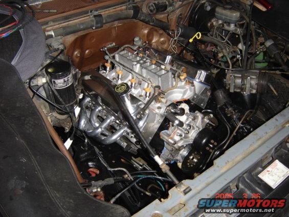 Engine bay showing a V8 engine with chrome headers and fuel injection. Oil filter and brake fluid reservoir visible
