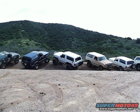 Several 1993 Ford Bronco SUVs parked on a dirt road with a hill in the background