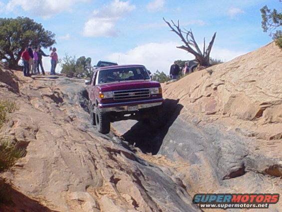 Red Ford F-Series truck climbing a rocky trail with people watching