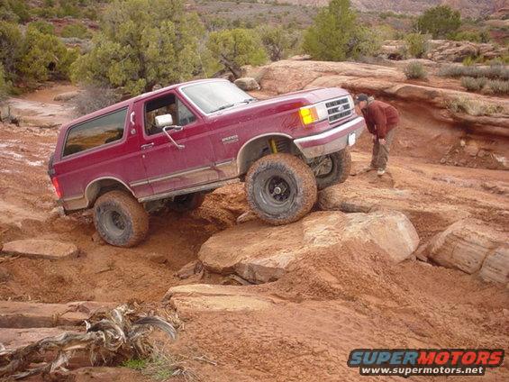 Red Ford Bronco off-roading on rocky terrain, front right tire elevated