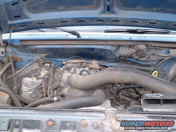 engine bay with hoses and engine parts visible, some text on a part reads '12/92'