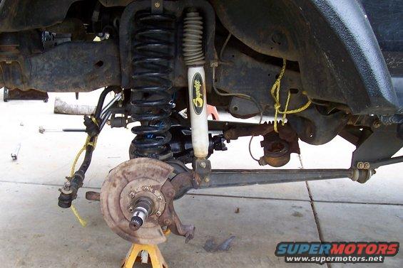 Front suspension components including coil spring, shock absorber, steering linkage, and brake rotor assembly on a yellow jack stand