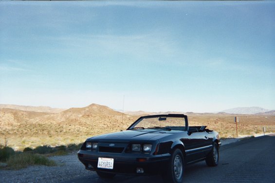 Black convertible parked on roadside with desert mountains in background. License plate reads 4GYU851