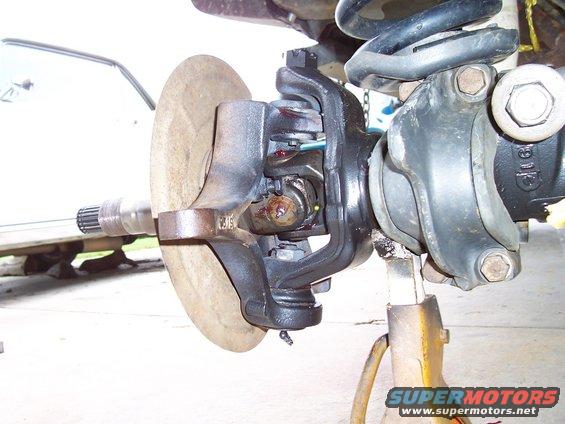 Close-up of a vehicle's front axle and suspension assembly, including a brake rotor and CV joint