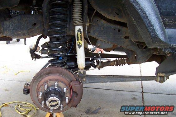 Front axle and suspension of a 1994 Ford F-150, showing a disc brake rotor, caliper, shock absorber, and coil spring