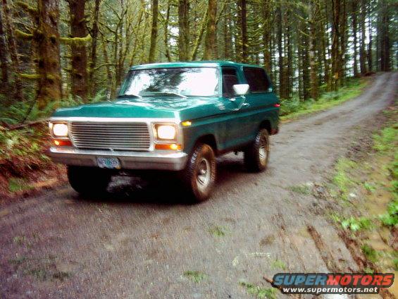 Green 1978 Ford Bronco driving on a muddy forest road
