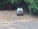 1978 Ford Bronco - Rear view of a 1978 Ford Bronco on a dirt path, surrounded by trees.