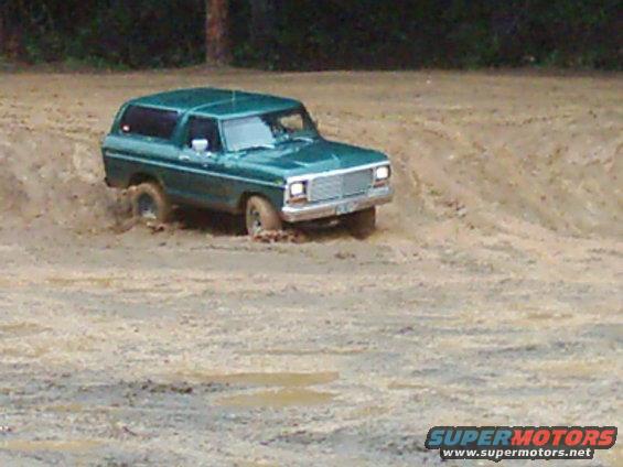 Green 1978 Ford Bronco driving through a muddy track