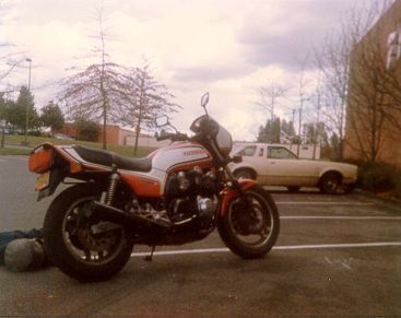 Red and white Honda motorcycle parked next to a beige car