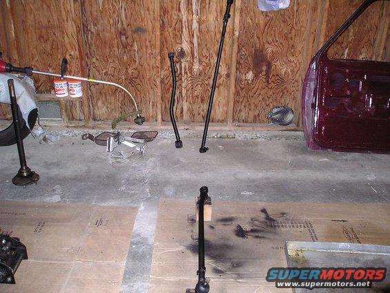 Maroon car door and various black steering linkage rods on a garage floor