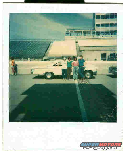 Four people stand next to a white 1963 Ford Galaxie at a racetrack