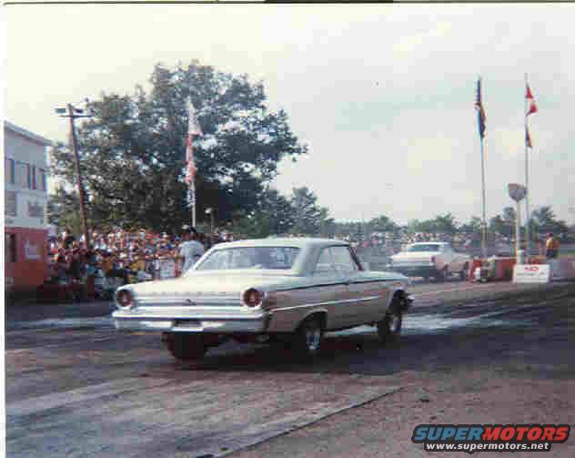 Car at drag strip, crowd watching, flags flying