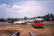 1957 Ford Deluxe - A drag strip scene with several cars and trailers under a partly cloudy sky.