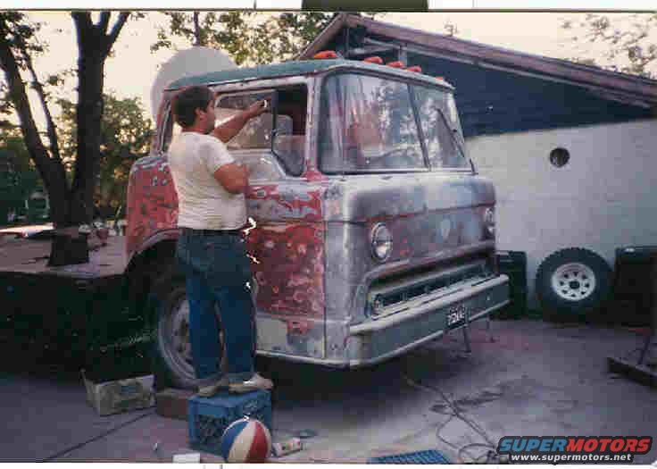 Front view of a truck with peeling paint, a man works on the driver's side