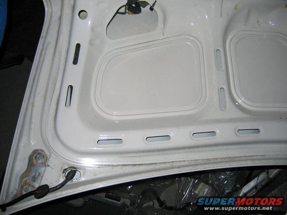 underside of a white car hood with stamped reinforcement ribs and wiring harness