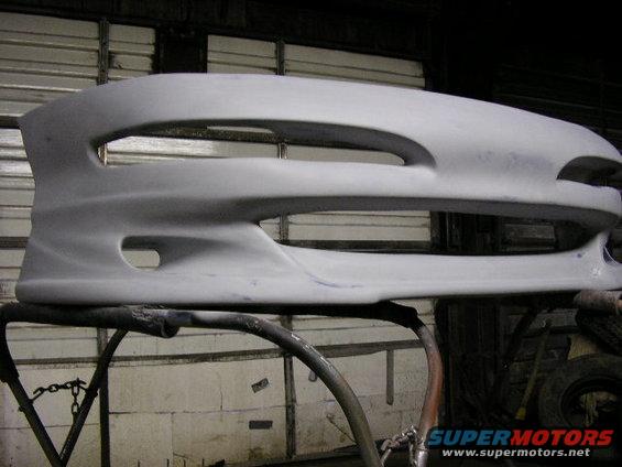 Unpainted car bumper on a stand, showing large central grille opening and two smaller side openings